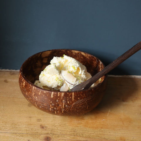 alt="no churn pina colada ice cream served in an organic coconut shell bowl with reclaimed wooden spoon. Recipe and bowl gift set available from Bramble and Fox UK hygge homeware shop"
