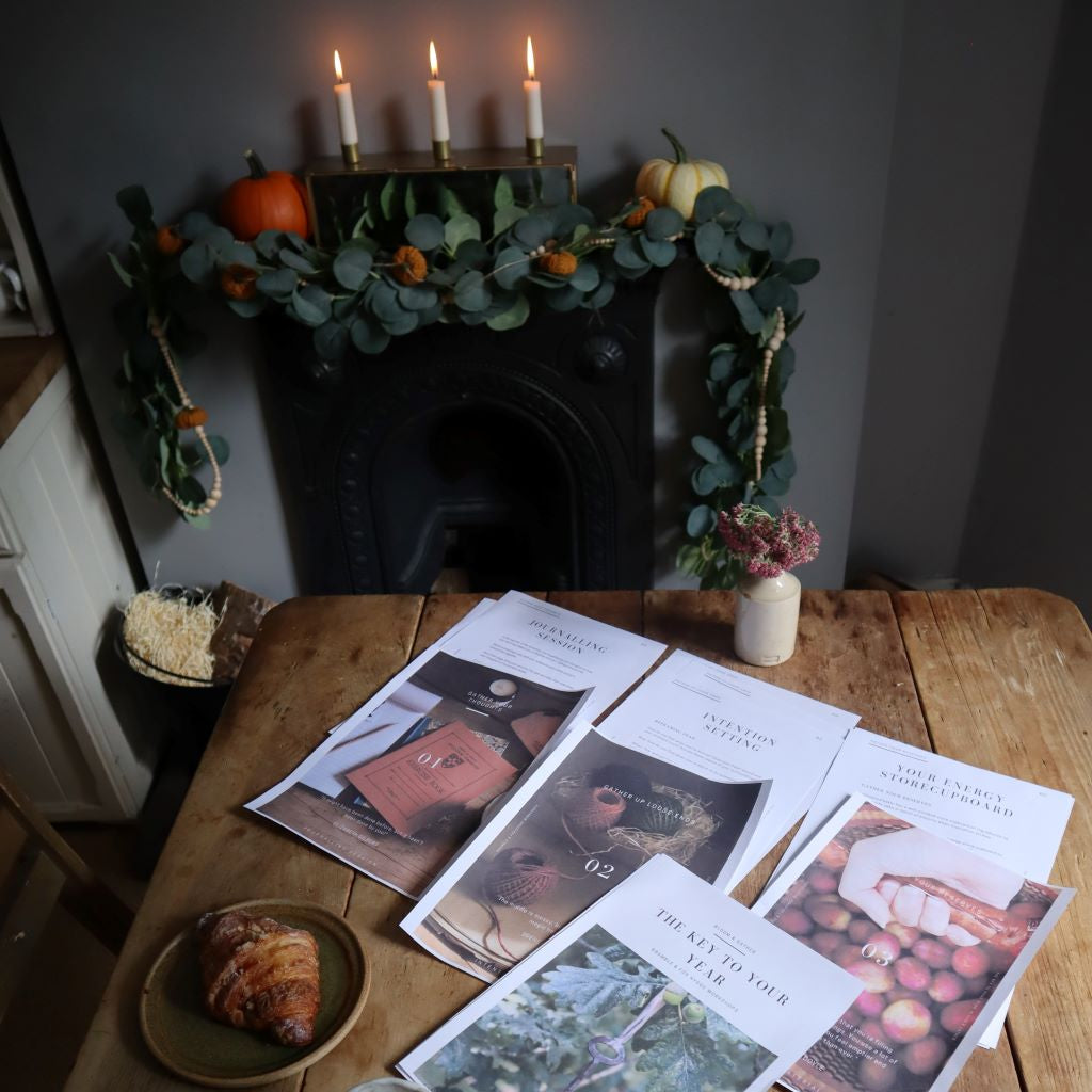 alt+"cosy flatlay of hygge workshop materials on table next to fireplace decorated with pumpkins and autumn decor. Hygge workshop available at Bramble and Fox UK hygge shop."