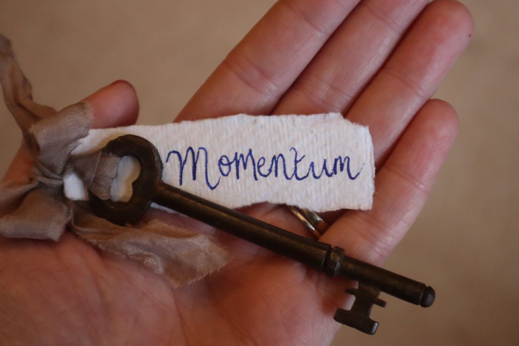 open hand with key and handwritten label which reads 'momentum'. Word for the year by bex massey of bramble and fox