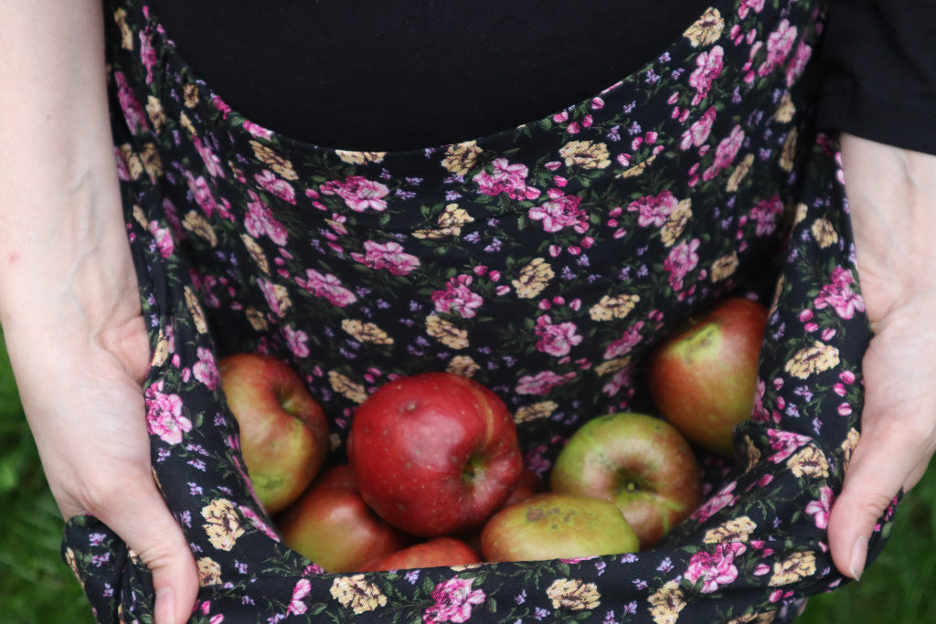 alt="woman's hands holding rosy apples in folds of hitched up skirt. Image by Bramble and Fox UK hygge cottagecore shop"