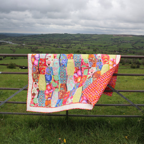 alt="patchwork quilt on a farm gate with fields in background. Available from Bramble and Fox UK hygge cottagecore shop"