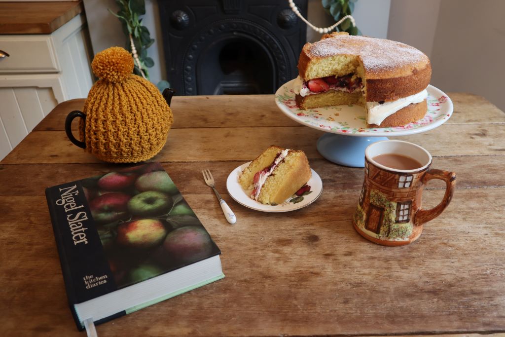alt="cosy tablescape of teapot, cake, mug and book from Bramble and Fox Uk Hygge shop and blog"