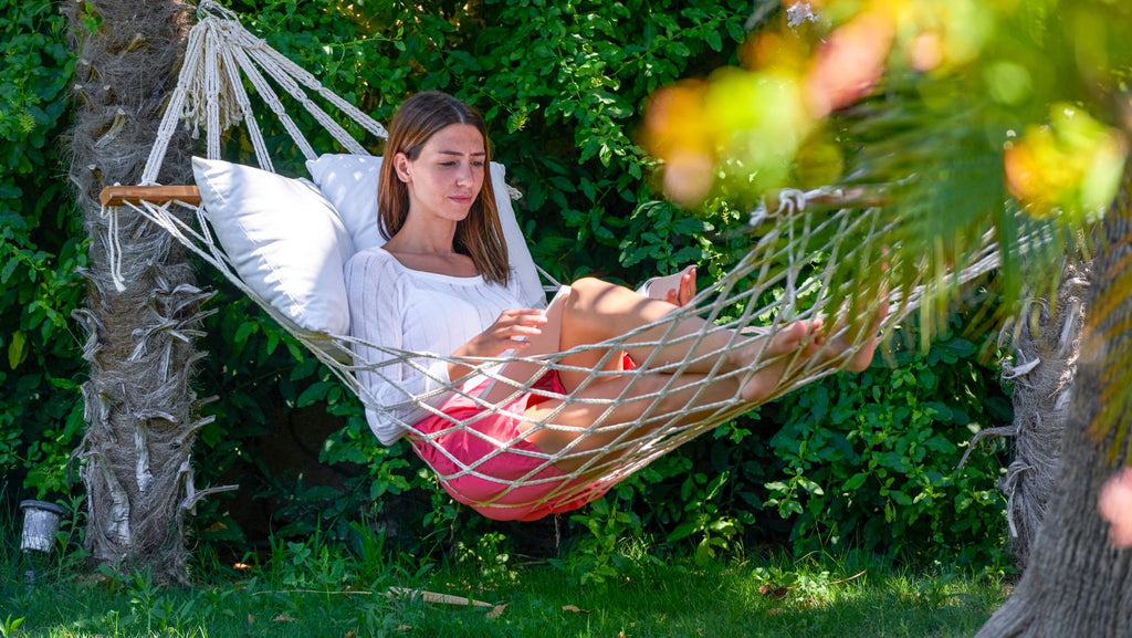 A young woman on a hammock reading a book in the garden