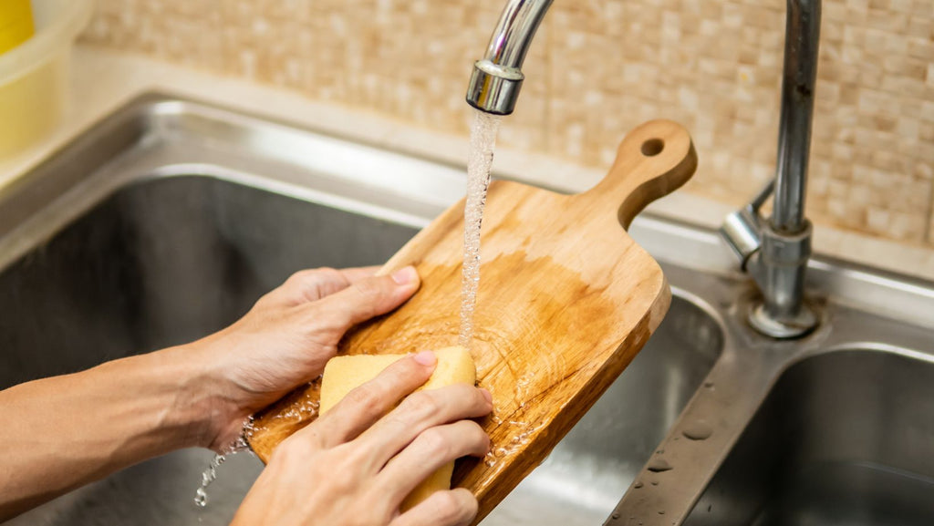 A person cleaning a butcher block in the kitchen sink