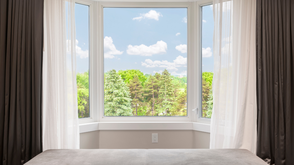 A bay window adorned with white curtains from inside a house