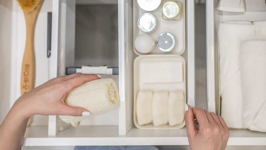 Top view of woman hands neatly organizing bathroom amenities and toiletries in drawer in bathroom