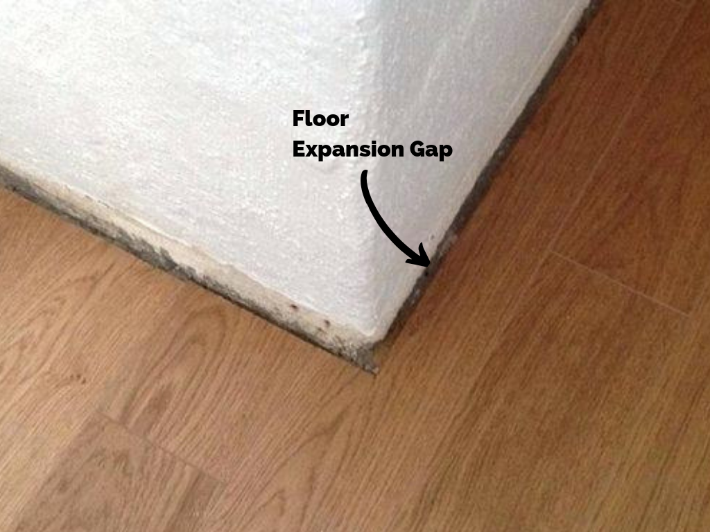 Hardwood floor 1/4'' expansion gap against drywall corner for baseboard trim installation.