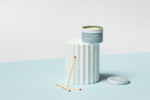 A medium jasmine & honeysuckle fragranced soy wax candle sitting atop a white plinth surrounded by scattered matches.
