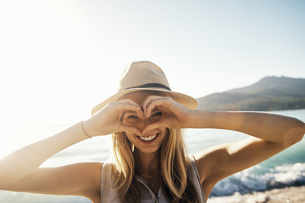 Woman smiling creating love heart sign in front of eyes at the beach