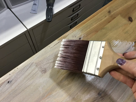 person using paintbrush to apply white wash solution to a cabinet