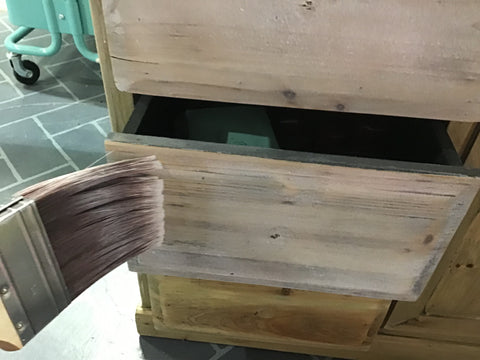 person applying white wash to the drawer fronts of a cabinet using a large paint brush
