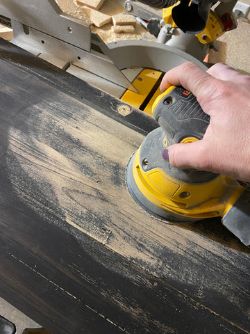 close up of person using orbital sander to sand off black paint from top of a cabinet