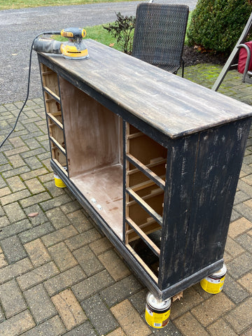 black cabinet with drawers and doors removed sitting outside on a brick patio raised up on paint cans