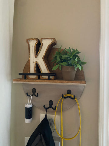 round wall shelf styled with a chunky "K", small faux green potted plant and dog leash and black jacket