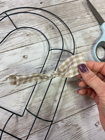 one beige and white gingham ribbon tied in a knot around a heart shaped wire wreath form ring