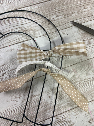 three coordinating neutral colored ribbons tied in knots around one ring of a wire heart shaped wreath form