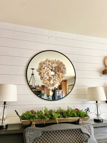 round mirror hanging on a shiplap wall with rag wreath hanging in front of the mirror