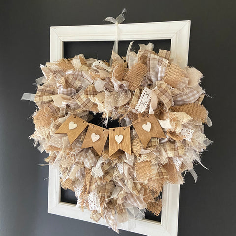 neutral colored heart shaped rag wreath hanging on wall on top of a white open frame and black painted wall