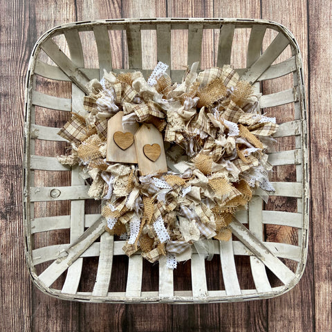 completed rag wreath in beige and tan and cream layered on top of a tobacco basket on top of a brown planked background