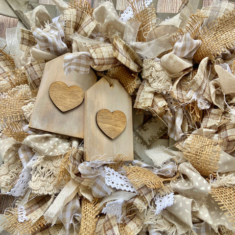 close up of rag wreath done in neutral beiges and whites and cream ribbons with mini tags embellished with hearts laying on top