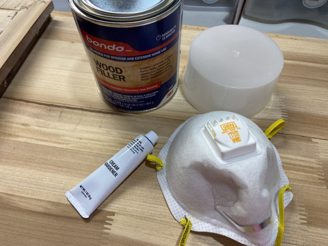 can of bondo and a dust mask sitting atop the bare wood top of a sanded down cabinet