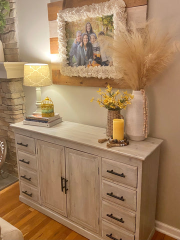 white washed cabinet with farmhouse modern hardware where the cabinet is sitting in front of a beige wall and styled with yellow and neutral vases and a lamp