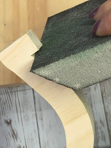 person's hand holding a sanding block to sand the side of a wooden horse shoe