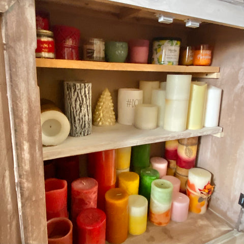 lots of candles color coded inside of a cabinet on three different shelves