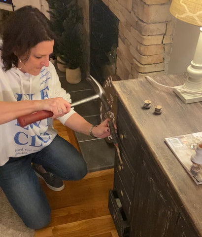 woman using hammer and putty knife to remove knobs on black cabinet