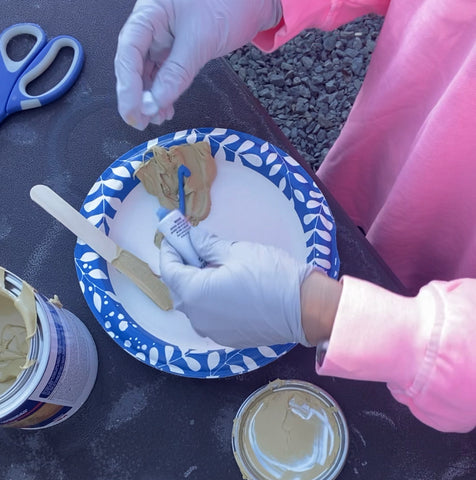 person mixing the two components of Bondo on a paper plate