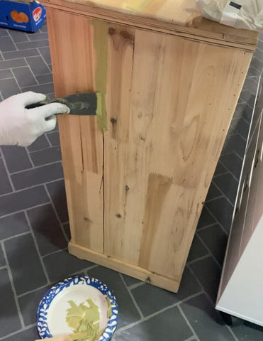 person applying Bondo with a putty knife to a large crack down the side of a bare wood cabinet