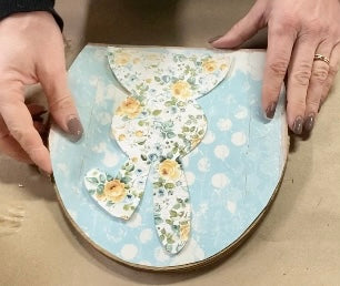 two layers of spring blue and yellow scrapbook paper on top of each other in preparation to decorate a wooden egg