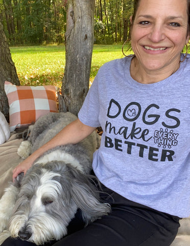 fluffy dog and woman sitting on picnic blanket where woman is wearing a shirt that says "Dogs make everything better"