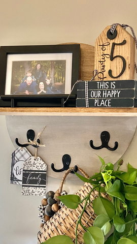 round shelf hanging on wall where shelf is holding a family photo in black frame, some small black books and the hooks are holding a wicker pitcher with greenery hanging down