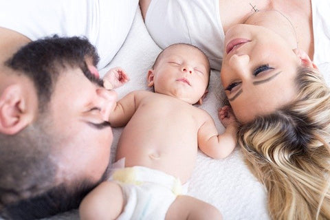 man and woman laying on bed upside down with a baby in a diaper in between them