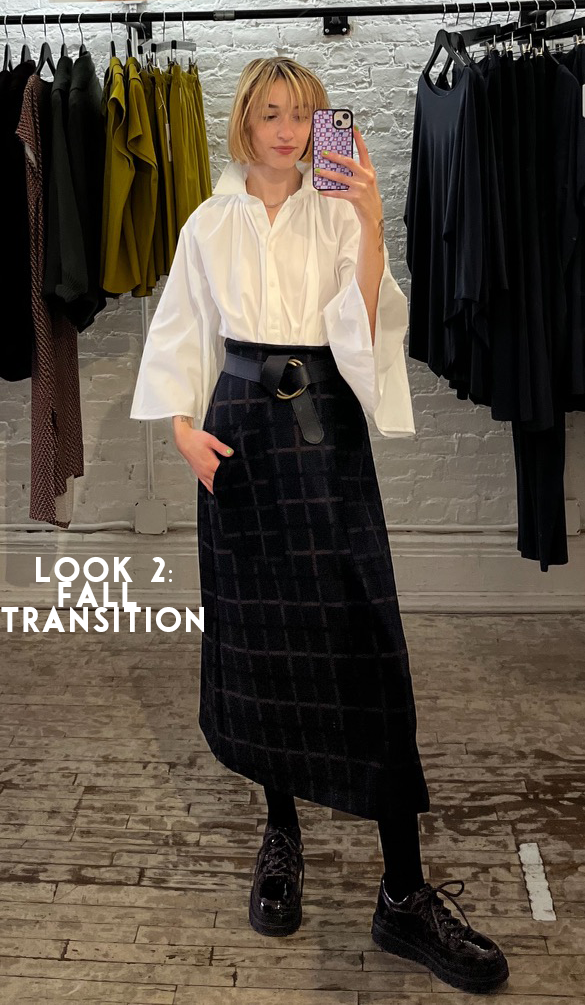 Leah transitioning a summer outfit to fall by wearing the Gathered Neck Dress in white, tucked into the Natalie Skirt, with black tights and chunky black shoes.
