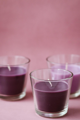 Three Finished Candles in the Color Purple Placed on a Pink Surface