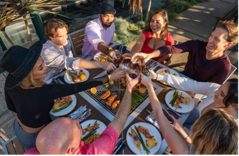 People toasting over a modern outdoor dining table with grill