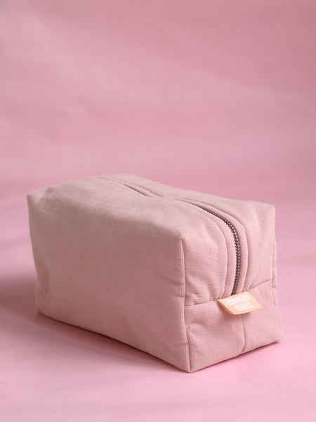 a light pink corduroy makeup bag on a pink backdrop