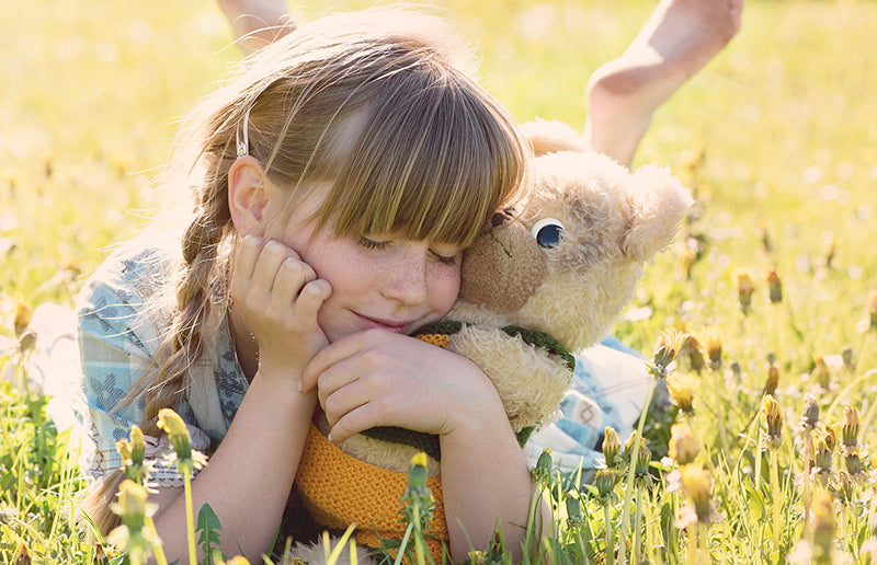 child-cuddling-with-her-teddy-bear-on-the-grass