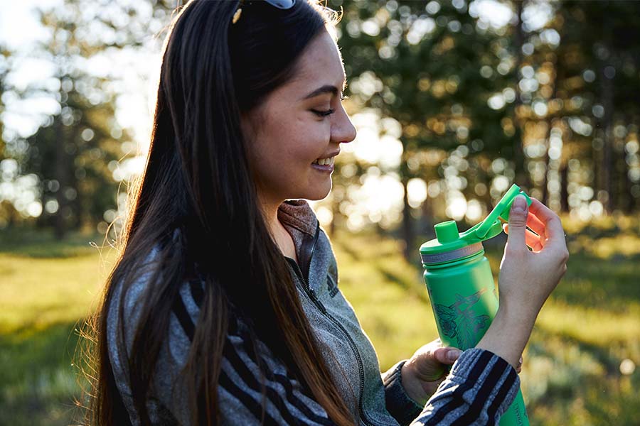 a girl is similing and looking at a water bottle with a built in tea infuser in the forest