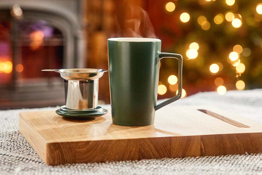 a green tea mug sits next to an infuser in front of a christmas tree and fire