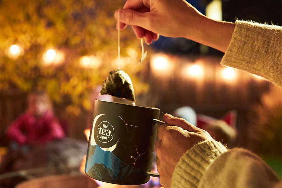 a person pulls a tea bag out of a nighttime themed mug in front of lights