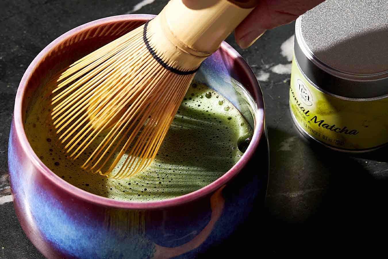 a matcha bowl has freshly brewed matcha while a matcha bamboo whisk is held above it