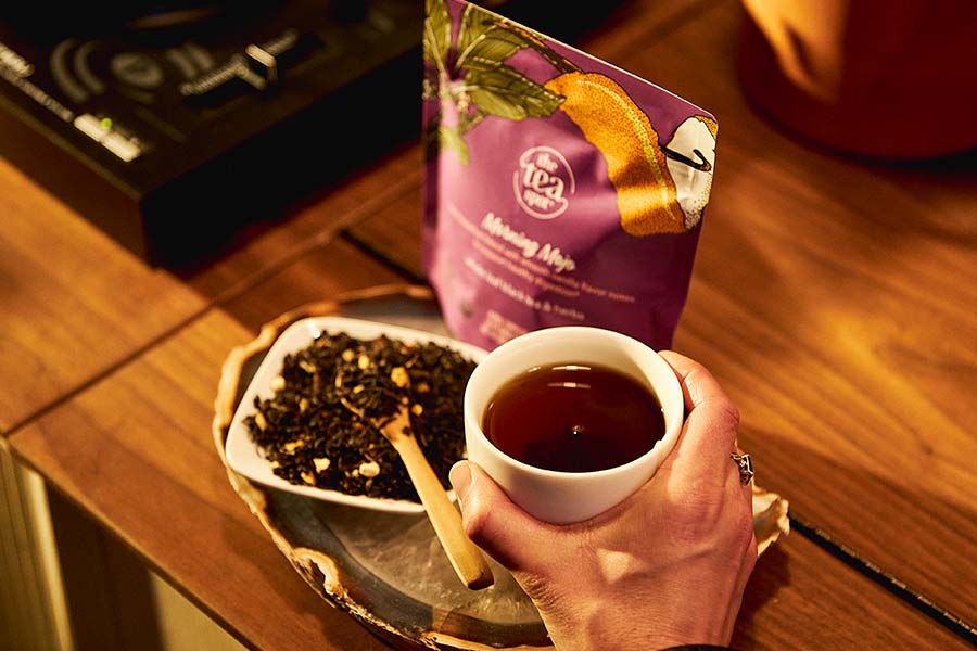 a tea mug is held over a table with a tea bag and loose leaf tea 