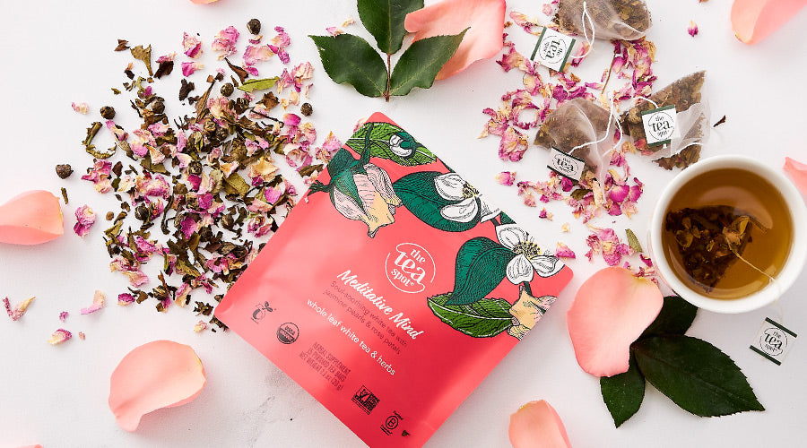 a pink pouch of white tea labeled meditative mind sits on a white background with rose petals