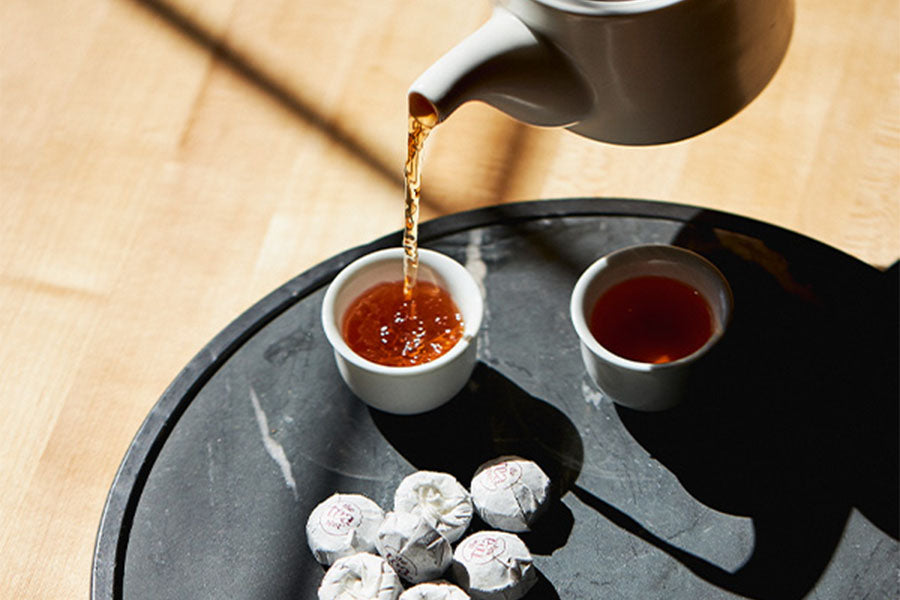 a teapot pours tea into a tea cup on a black tray