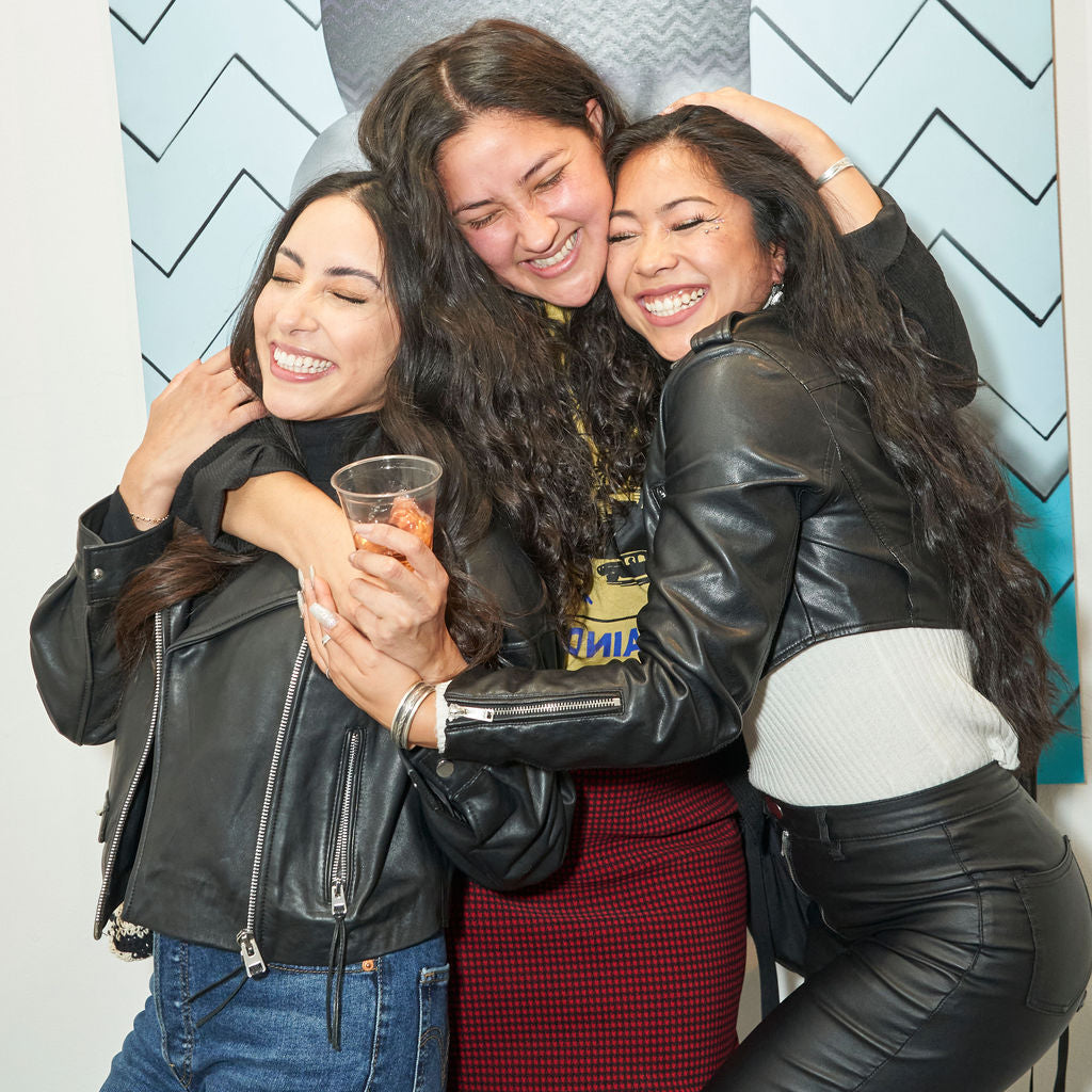 Photograph of three women hugging each other during Ernie Steiner's "Figuratively Speaking" solo exhibition Opening Reception at Voss Gallery, San Francisco, April 22, 2022.