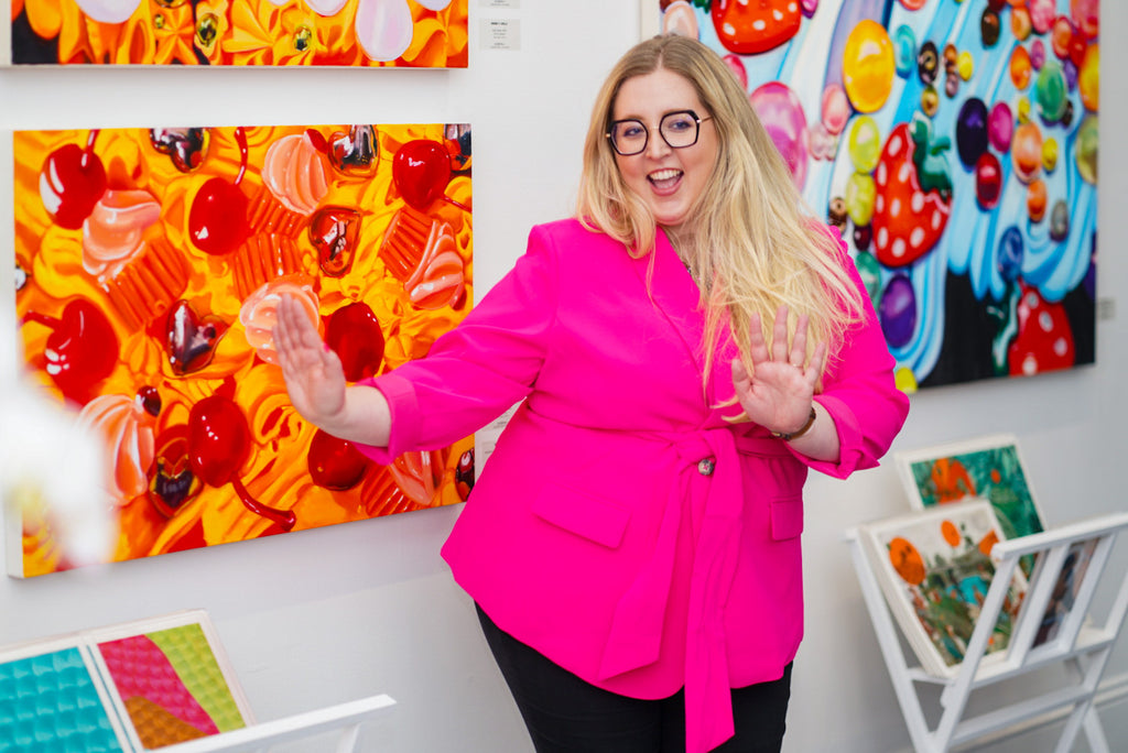 Vibrant San Francisco gallery scene with a woman in a bright pink blazer, joyfully presenting colorful contemporary art at Voss Gallery.