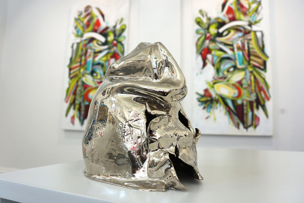 Photograph of a silver sculpture and artwork in the background during John Osgood's "In Plain Sight" solo exhibition at Voss Gallery Francisco, May-June 2020.